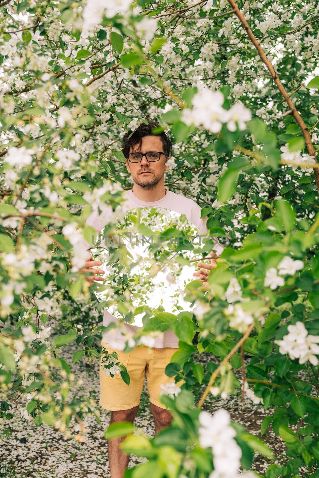 Creative male portrait with mirror in a blooming apples spring garden