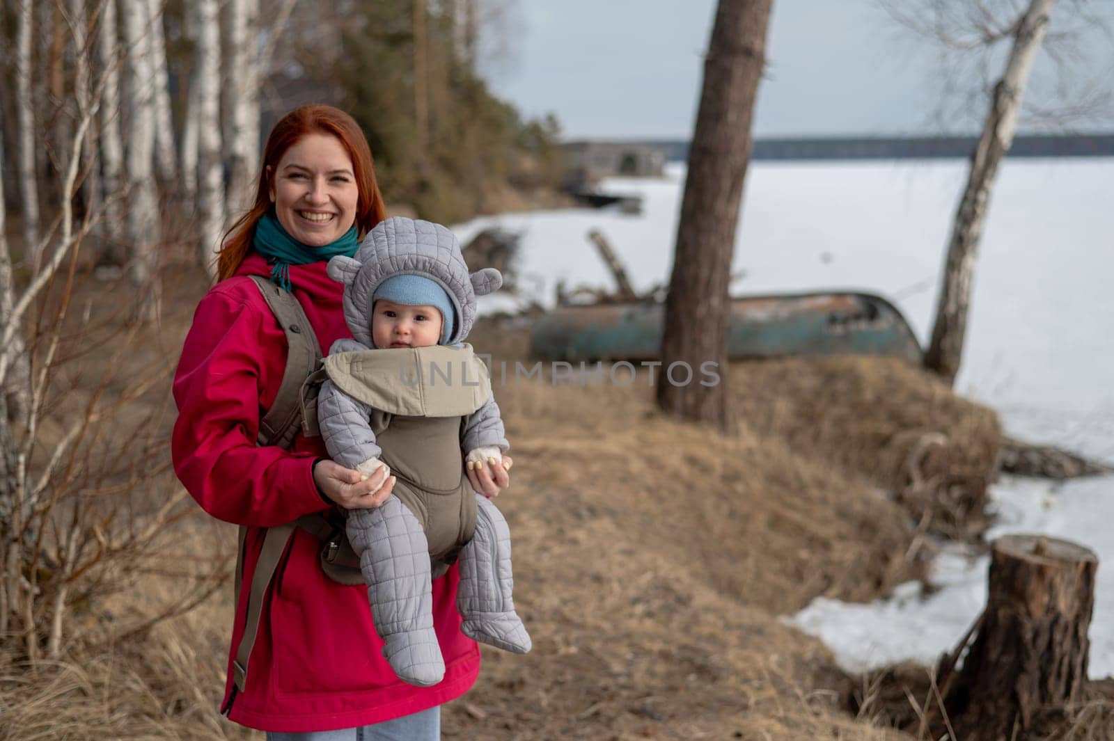Caucasian red-haired woman walks with her son in an ergo backpack in nature in winter. by mrwed54