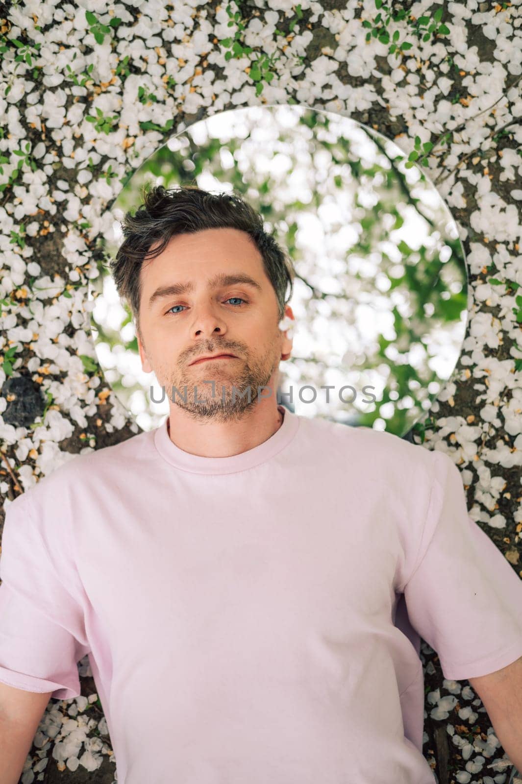 Creative male portrait with mirror lying in the ground in a blooming apples spring garden