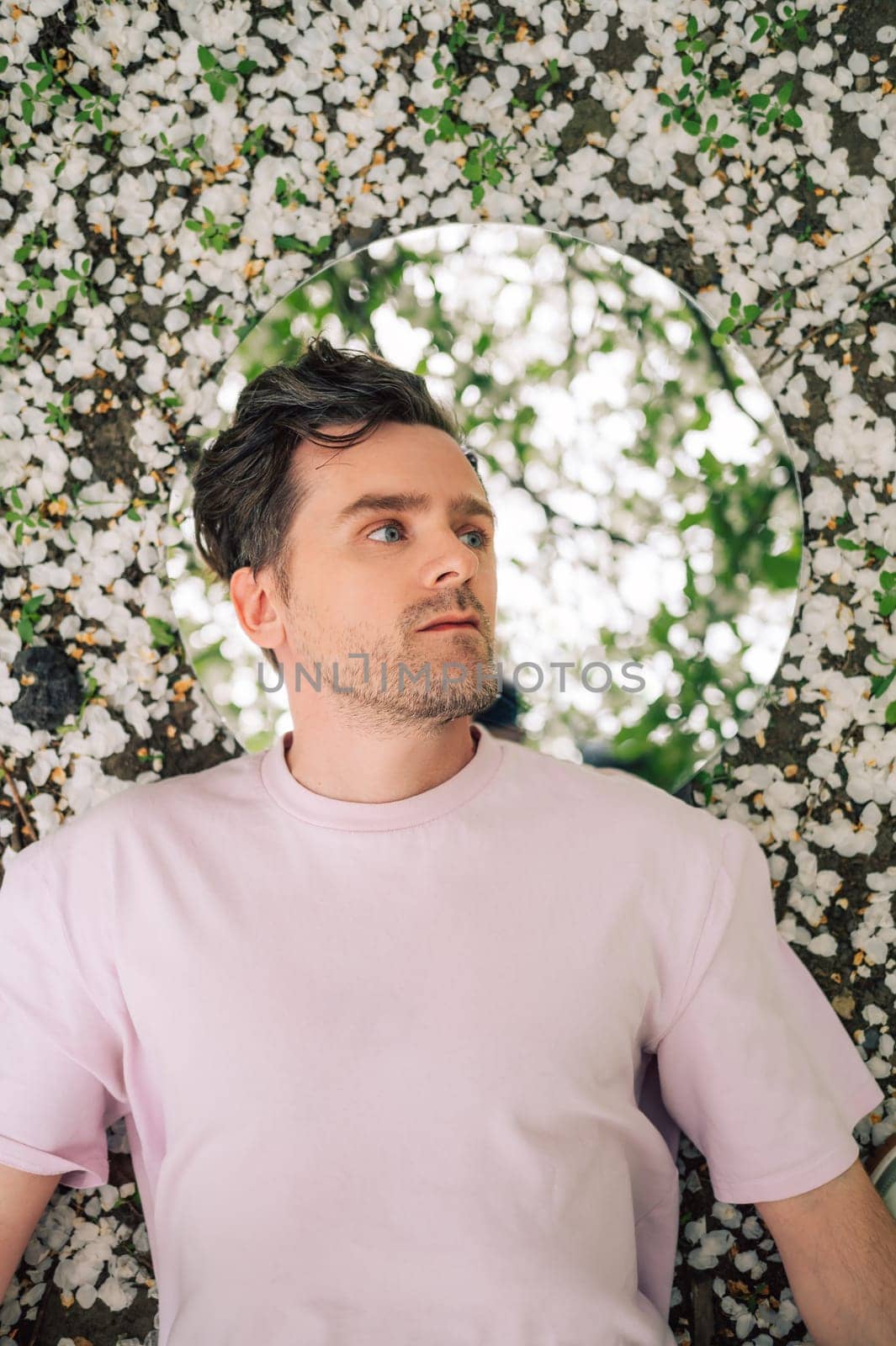 Creative male portrait with mirror lying in the ground in a blooming apples spring garden