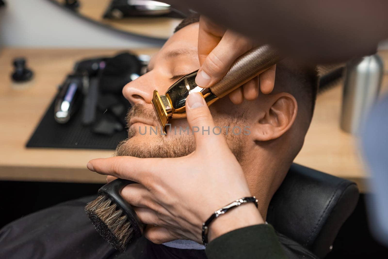 Barber maneuvers the trimmer along the clients cheek, carefully cutting and defining the beard
