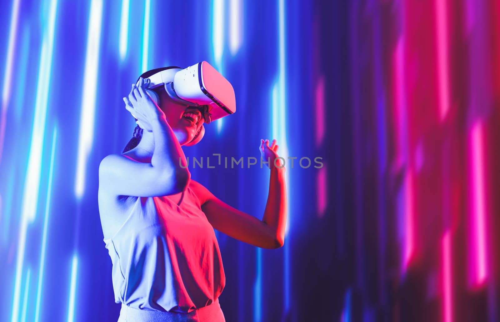Smart female standing surrounded by neon light wearing VR headset connecting metaverse, future cyberspace community technology. Elegant woman enjoy dancing wavering body and sing song. Hallucination.