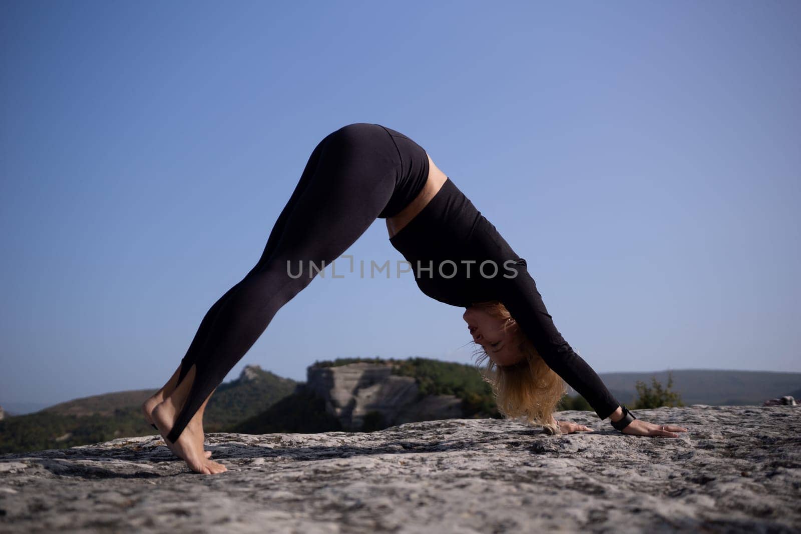 A woman is doing a yoga pose on a rocky surface. Concept of strength and determination as the woman stretches her body to its limits. The rocky terrain adds an element of challenge to the pose