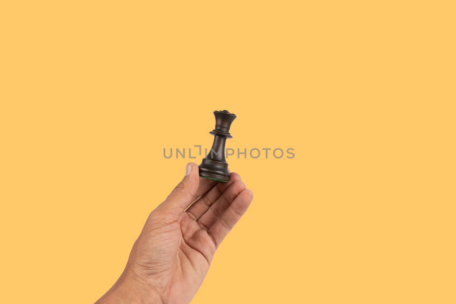 Black male hand holding a black queen chess figure isolated on yellow background. High quality photo