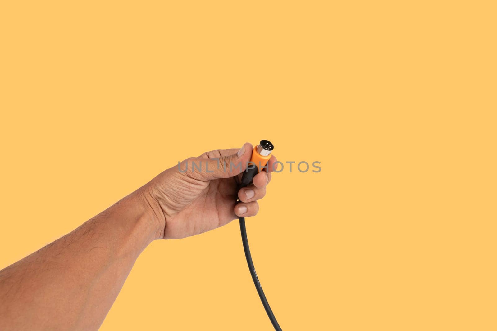 Black male hand holding a MIDI audio cable isolated on yellow background by TropicalNinjaStudio