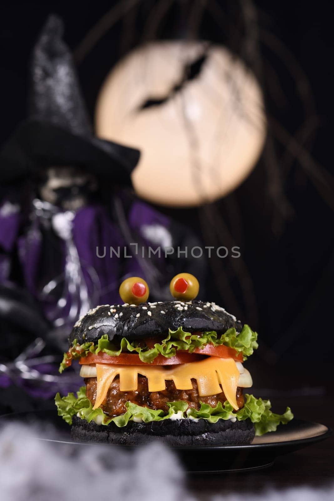Monster Burger. Black bun, juicy beef cutlet, lettuce, onion, tomato and cheese in the shape of teeth, eyes with olives. Definitely a pick-me-up and a perfect Halloween party appetizer.