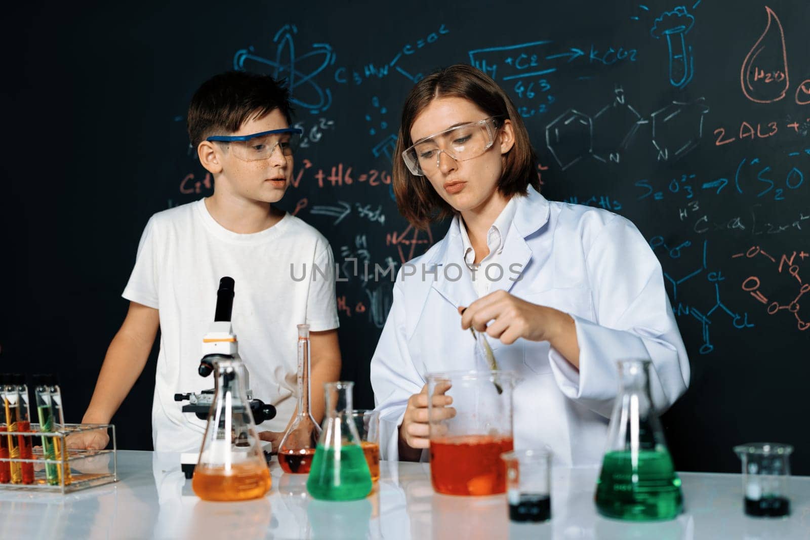 Teacher support schoolboy in laboratory. Schoolboy and teacher stand and experiment about science of chemistry in STEM class using liquid in glass container. Instructor mixing solution. Erudition.