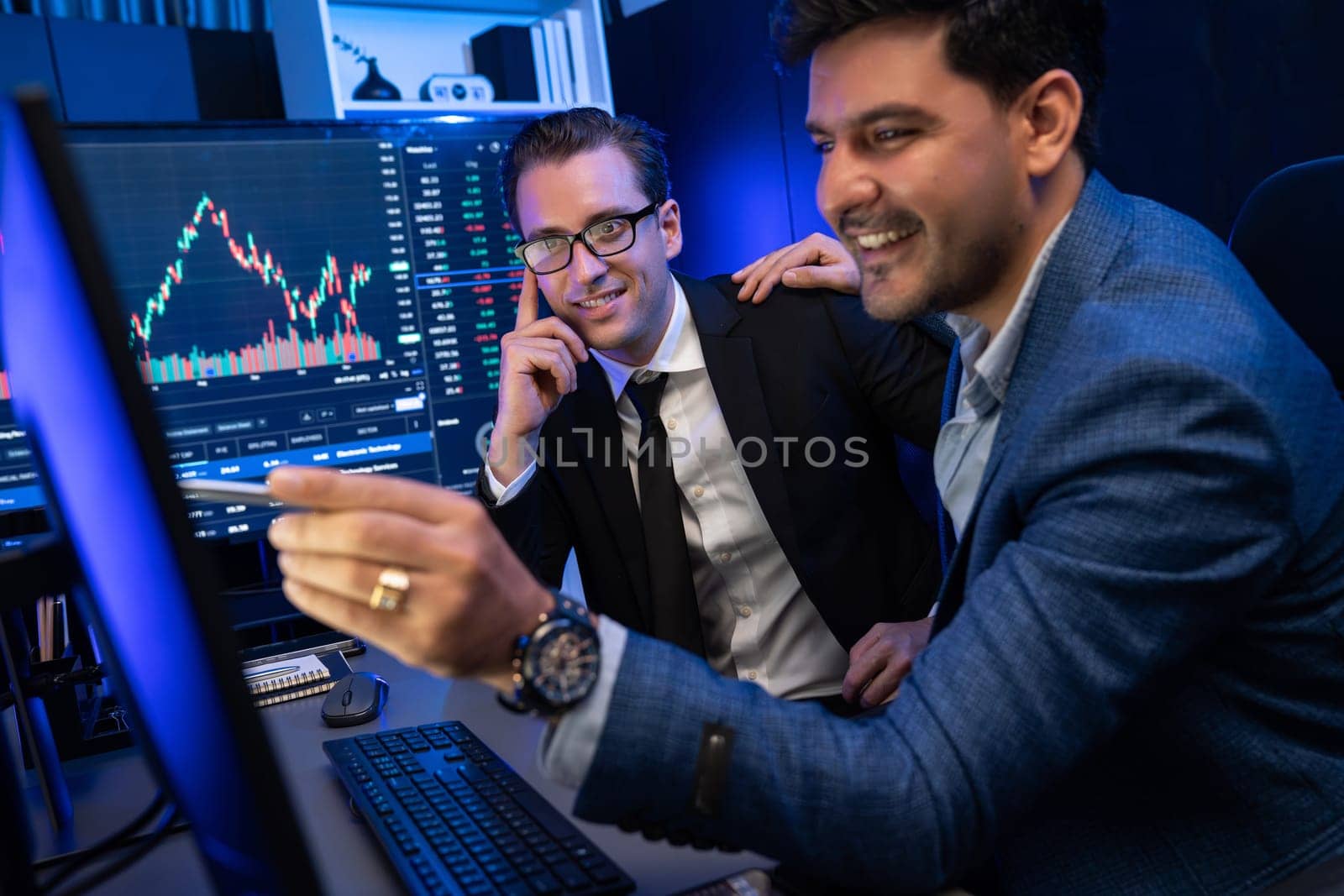 Two stock exchange traders discussing on dynamic successful investment graph, pointing trending of high profit in currency stock in financial data on monitor in neon light at workplace. Sellable.