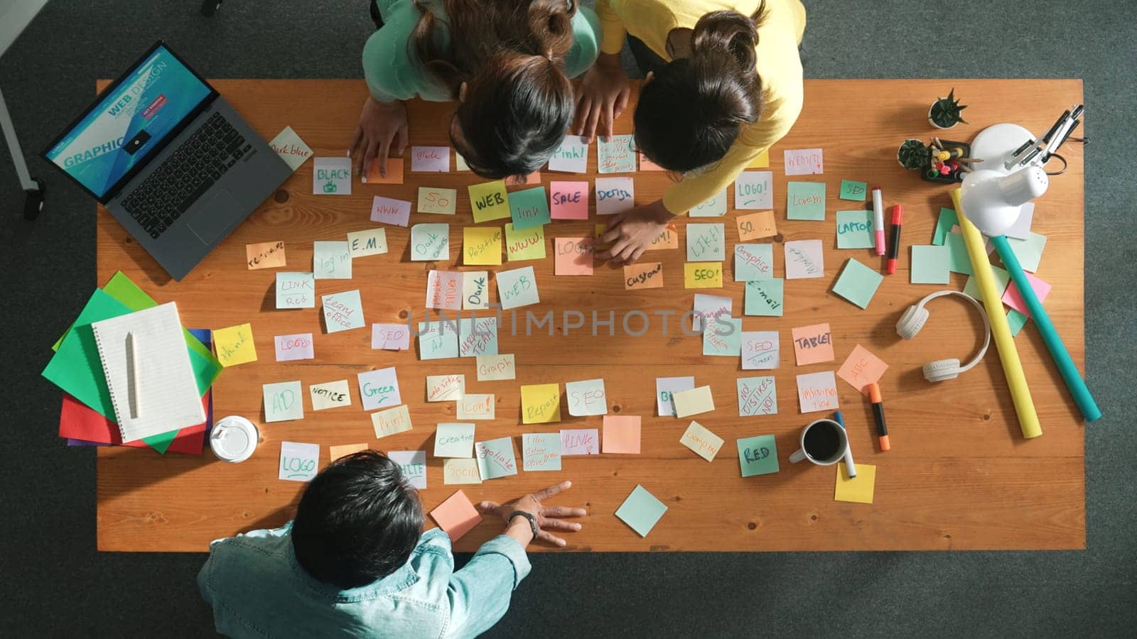 Top view of manager looking at idea on sticky notes and explain idea about web design. Skilled marketing team or programmer brainstorming idea while looking at tablet with color palette. Symposium.