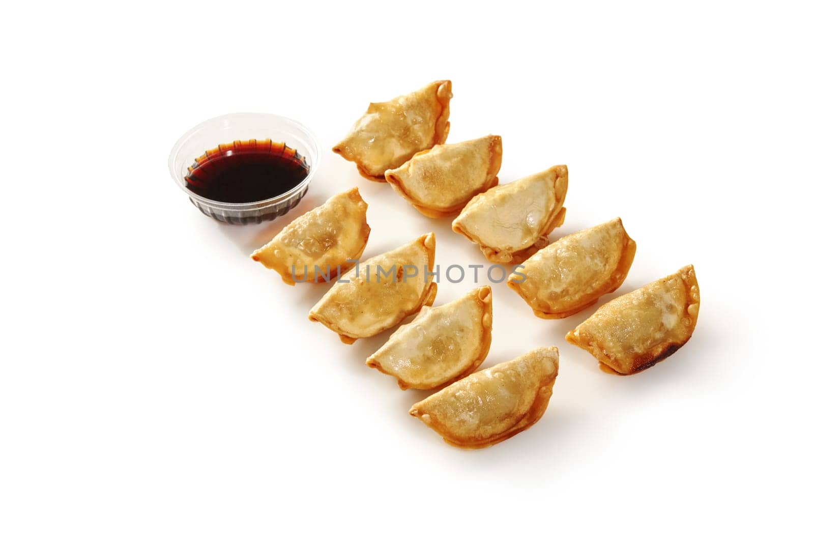 Appetizing golden gyoza, crispy pan-fried dumplings with savory filling traditionally served with cup of soy sauce, isolated on white background. Japanese style street food