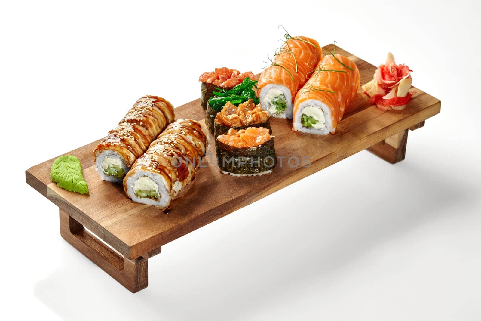 Delectable eel and salmon Philadelphia rolls and gunkan maki with various toppings served with wasabi and pickled ginger on wooden tray, isolated on white background. Japanese style lunch