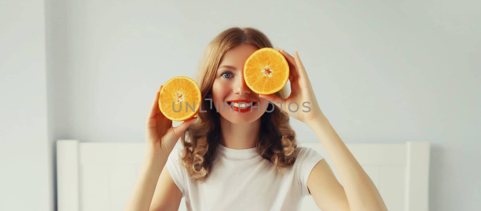 Summer, nutrition, diet and vegetarian concept. Happy healthy cheerful young woman with slices of orange fruits in white room at home