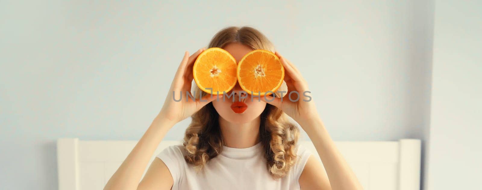 Summer, nutrition, diet and vegetarian concept. Happy healthy cheerful young woman covering her eyes with slices of orange fruits and looking for something in white room at home