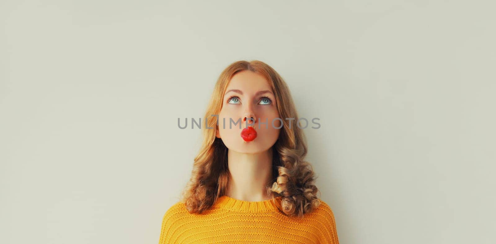 Pensive caucasian young woman thinks looking up, red lipstick, on studio background, blank copy space