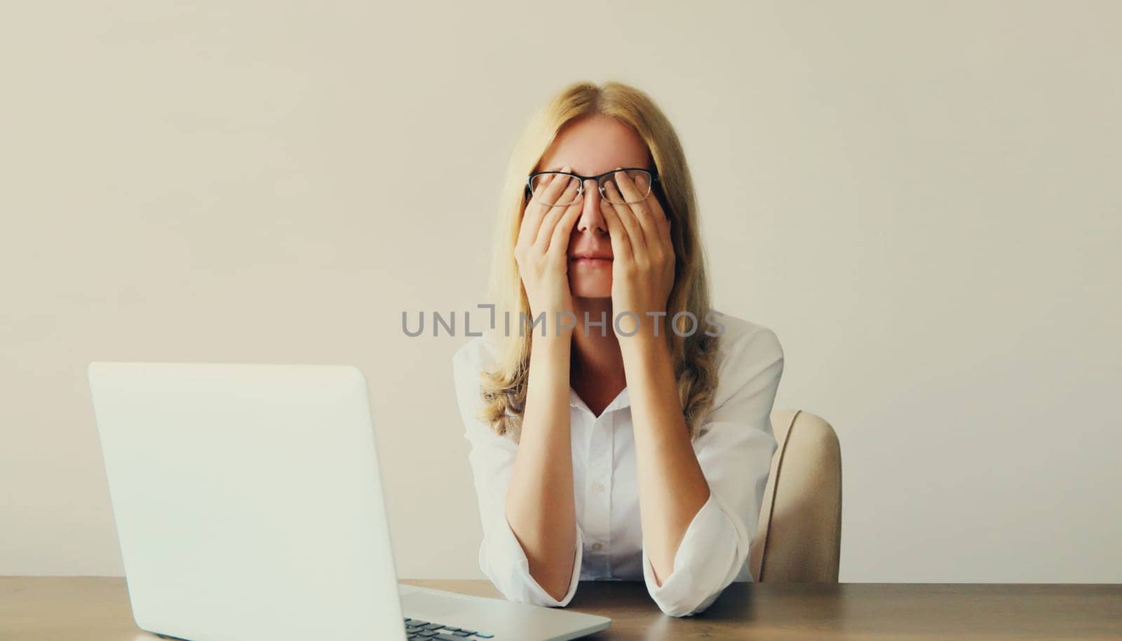 Tired overworked woman employee suffering from headache, rubbing her dry eyes, working with laptop sitting at desk in office