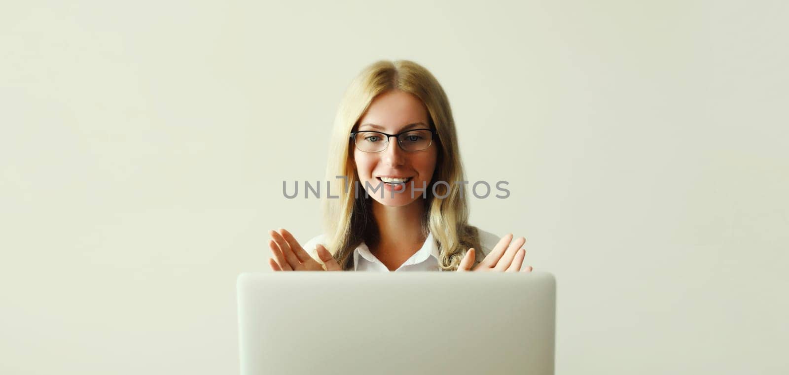 Happy young woman working on laptop greets communicates with friends via video call sitting at desk in office or home
