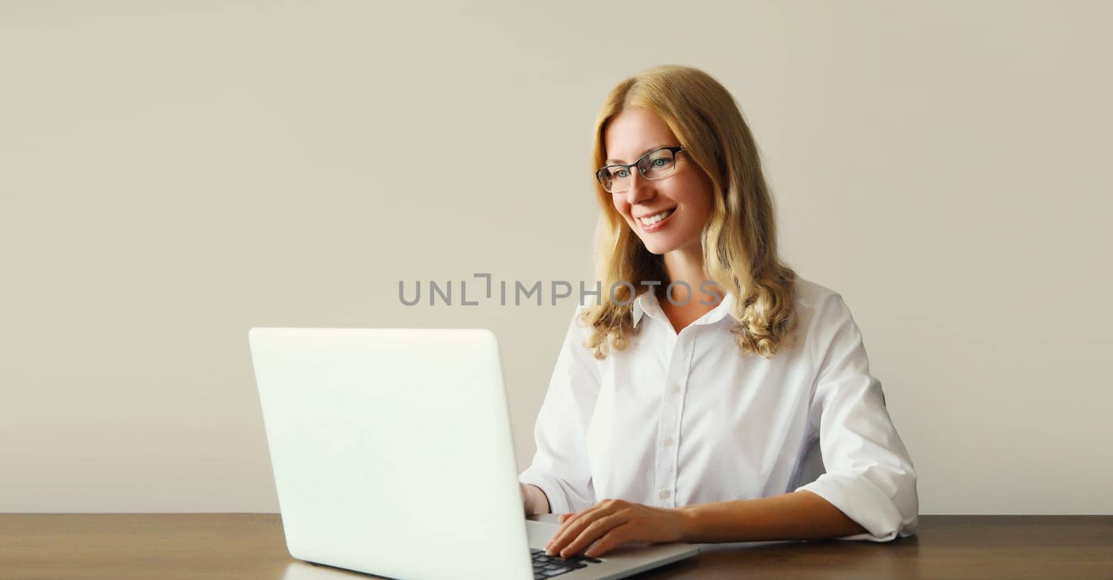 Happy woman working with laptop sitting at desk in office or home by Rohappy