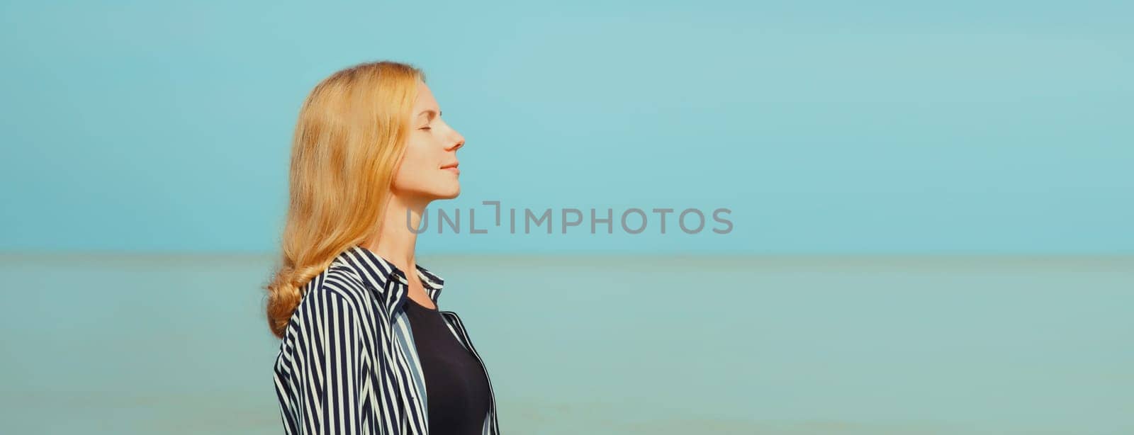 Calm relaxing healthy young woman meditates, practicing breathing exercises enjoying fresh air on the beach on sea coast and blue sky background