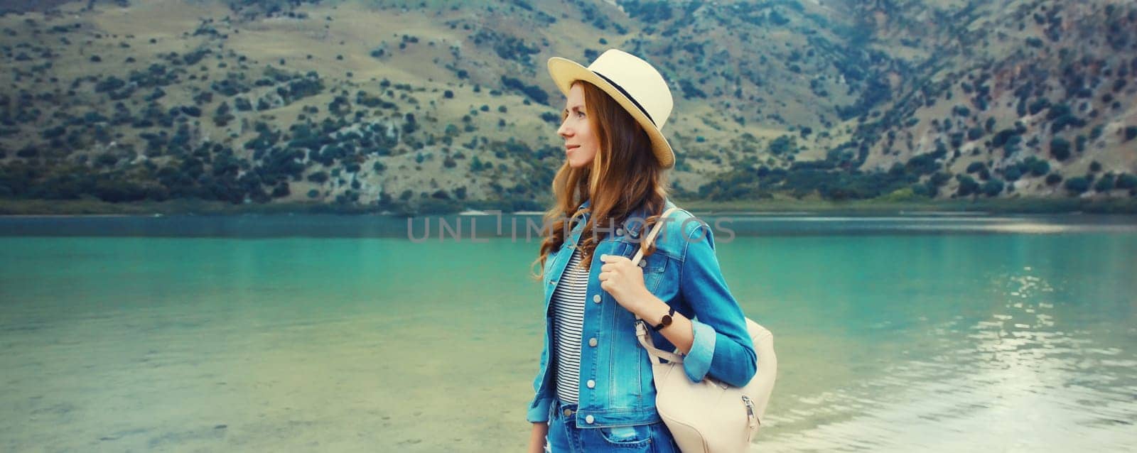 Summer vacation, young woman tourist in straw hat with backpack on lake and mountains background. Greece, island Crete