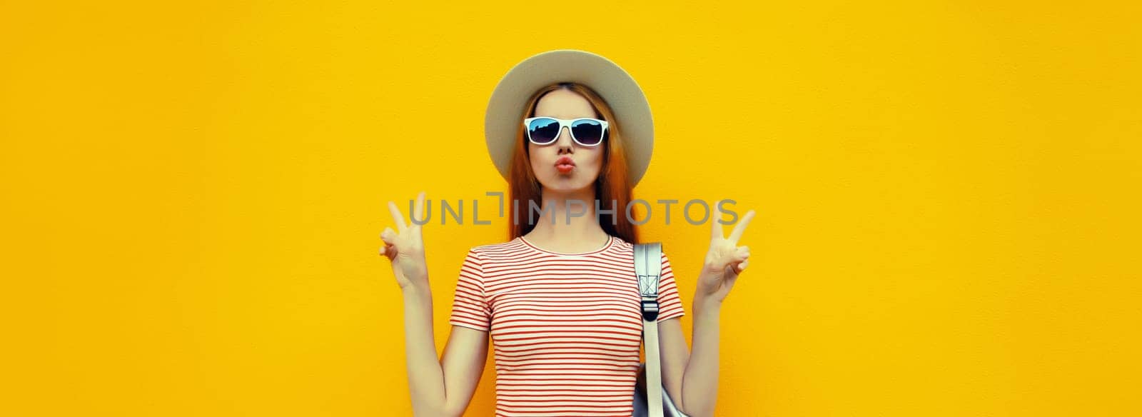 Portrait of stylish young woman posing in summer straw hat on bright yellow studio background