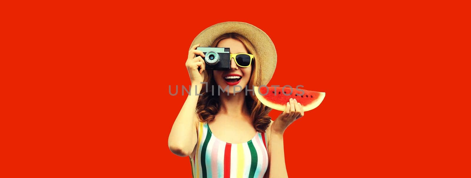 Summer portrait of happy smiling young woman with film camera and slice of fresh watermelon wearing straw hat on red background