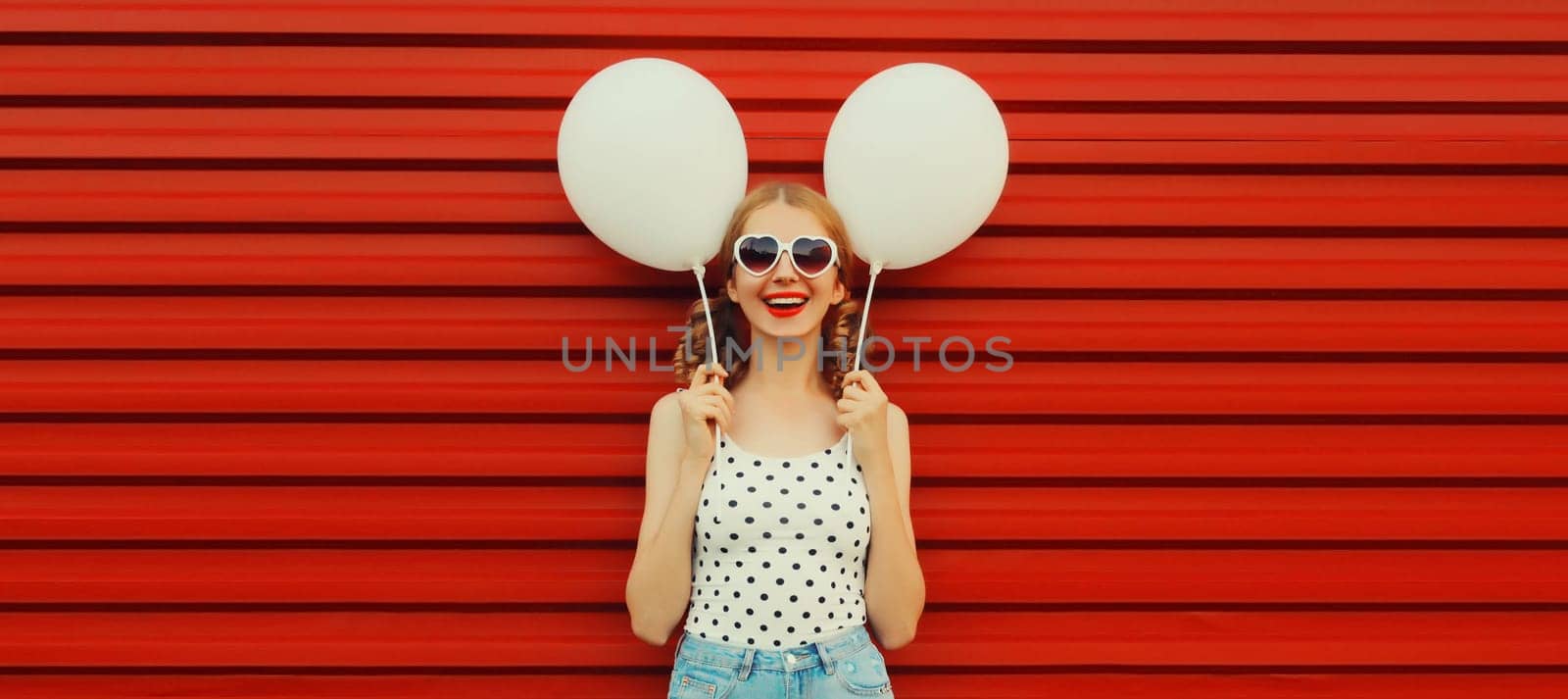 Summer, holiday, celebration, happy cheerful young woman with bright colorful balloons wearing white heart shaped sunglasses having fun on red background