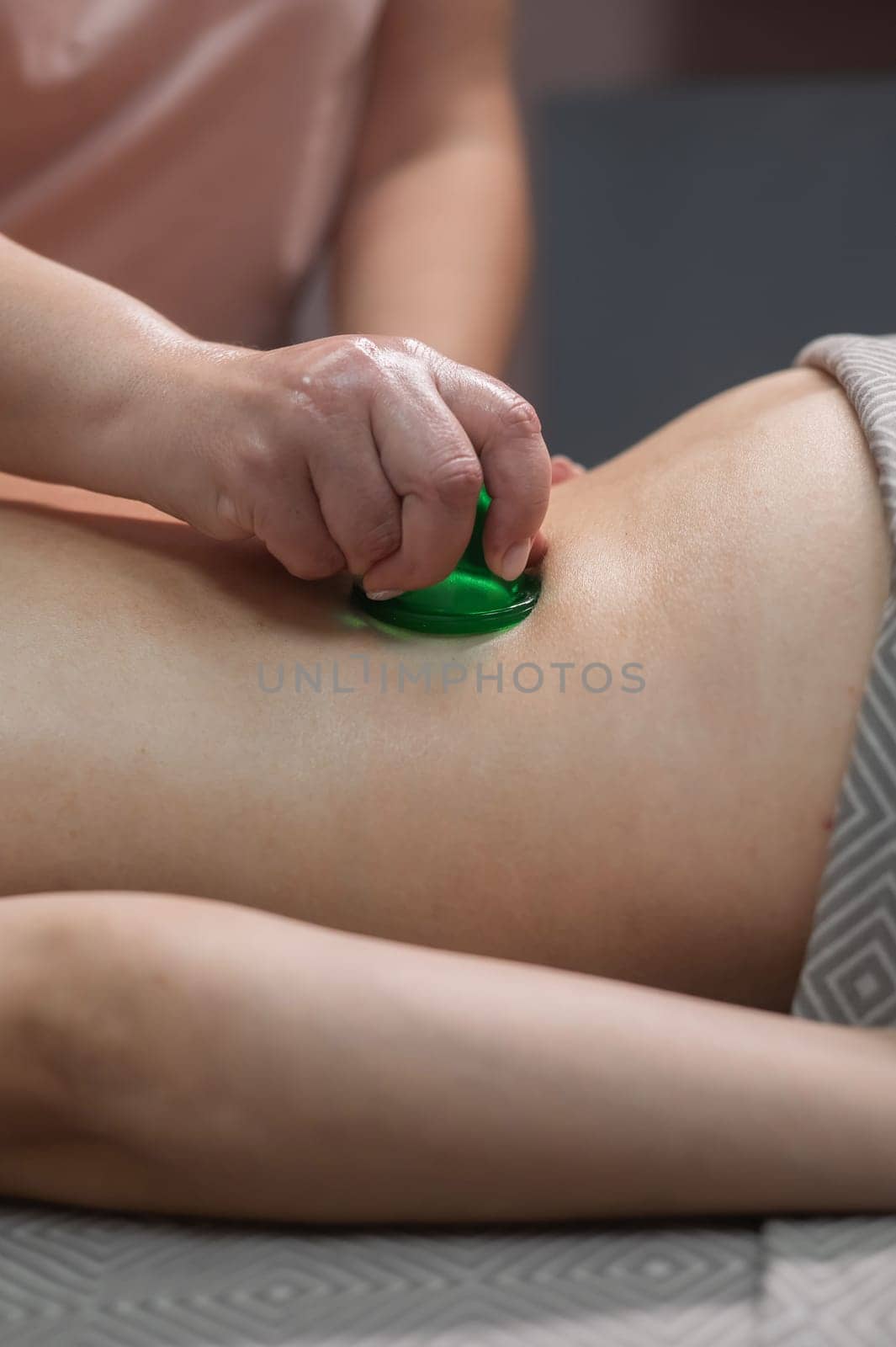 A woman undergoes an anti-cellulite massage procedure using a vacuum jar. Close-up of the lower back. Vertical photo