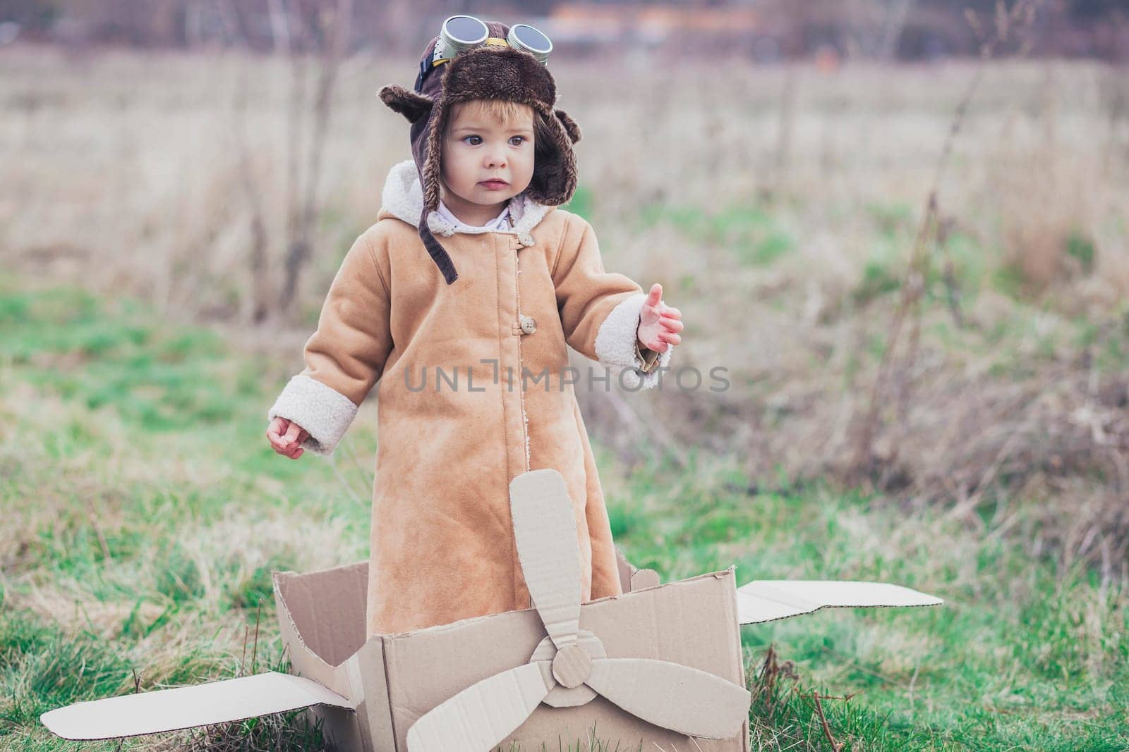 Charming baby in aviator's clothes on the cardboard plane.