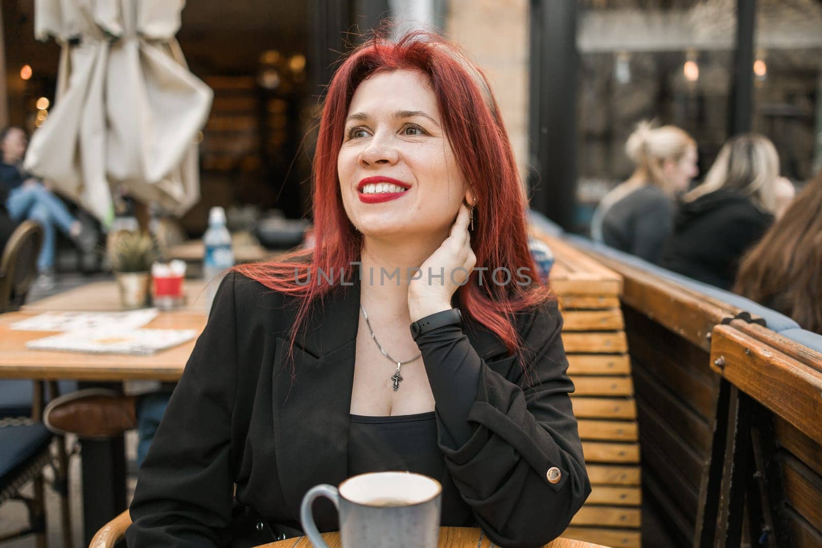 Beautiful happy woman with long red hair enjoying coffee in a street cafe by Satura86