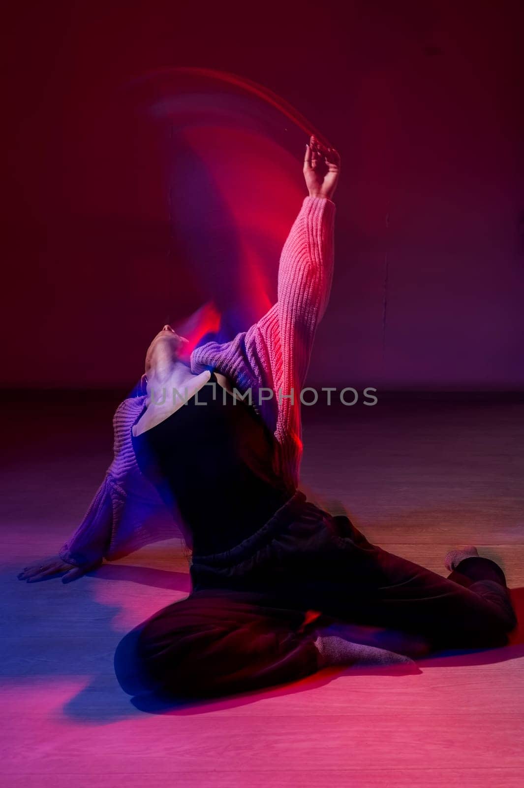 A young woman dances contemporary dances in blue and red light. Long exposure. Vertical photo