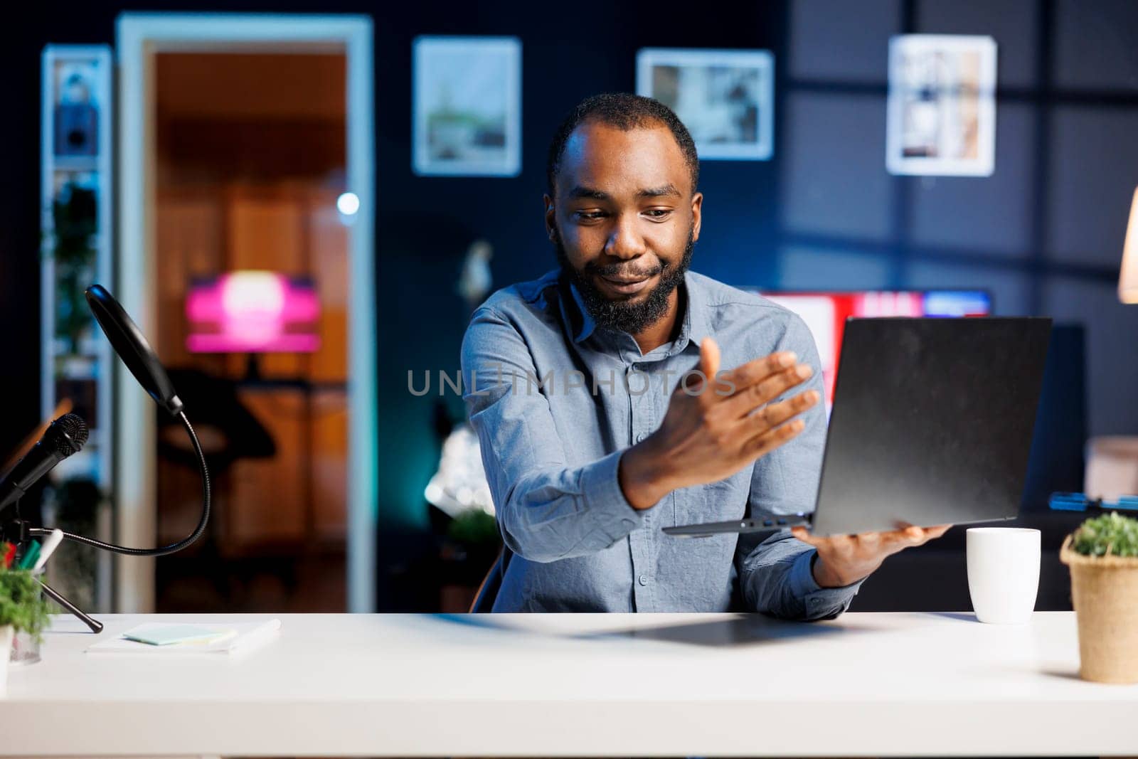 African American man assessing laptop, expressing dissatisfaction with subpar components quality. Content creator shooting video for online channel, displeased with notebook device performance