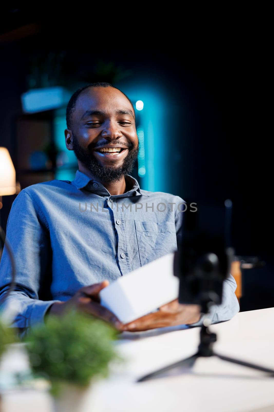 Cheerful content creator filming technology review of newly launched digital device, unboxing it and presenting specifications to audience. Internet star laughing while showing product to viewers