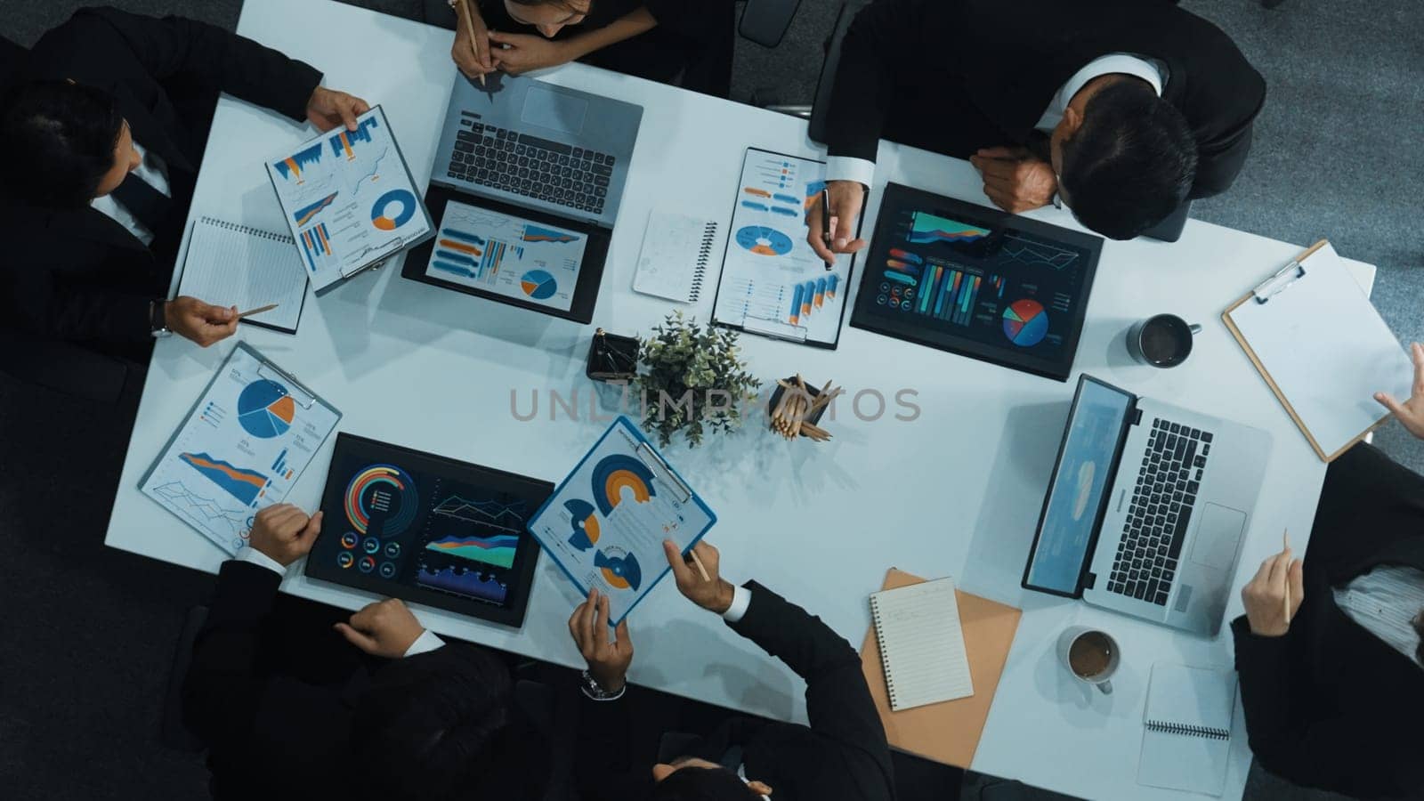 Top down aerial view of business people discussing about financial strategy on table with document and tablet display investment statistic at meeting. Diverse team brainstorm about plan. Directorate.