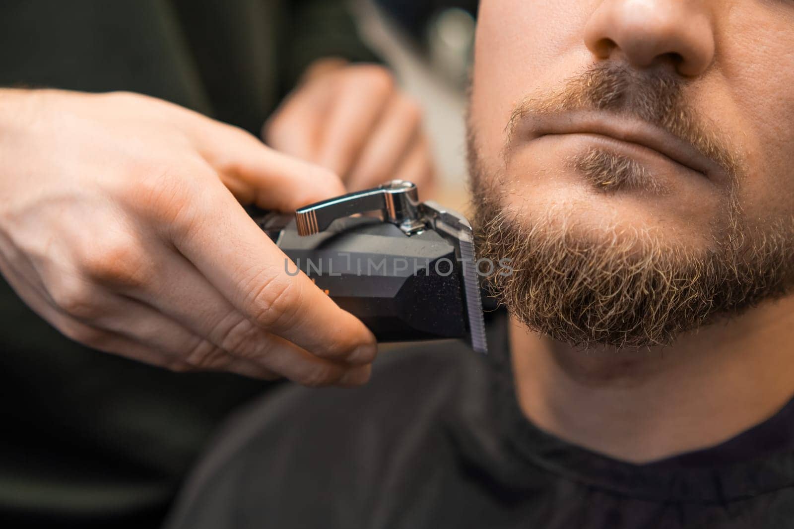 Barber hand trims clients beard with trimmer in the barbershop.