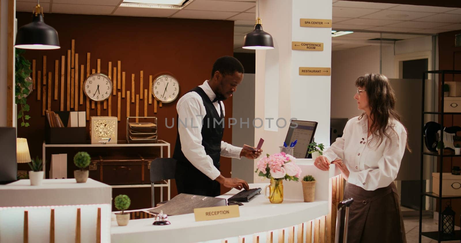 African american worker verifying passport id at front desk before registering for room reservation, concierge services. Staff assisting old woman with check in, hospitality industry.