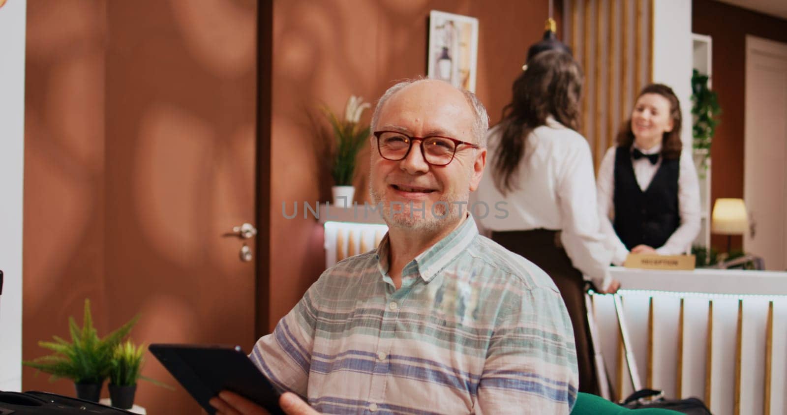 Senior person using modern tablet in hotel lobby, relaxing in lounge area before starting retirement holiday trip. Browsing online webpages to find recreational activities, leisure senior travel.