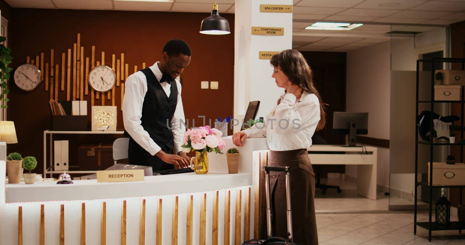 African american staff greets woman at hotel reception, assisting with check in process during retirement vacation. Senior person travelling on holiday, receiving luxurious concierge services.