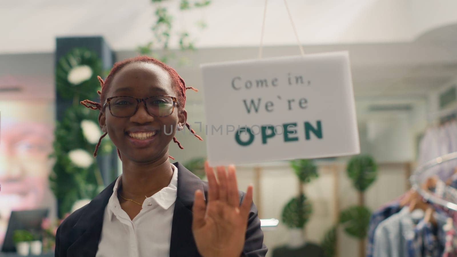 Portrait of cheerful BIPOC woman opening stylish fashion boutique, starting her shift in the morning. Employee turning closed sign on fast fashion clothing store into open one