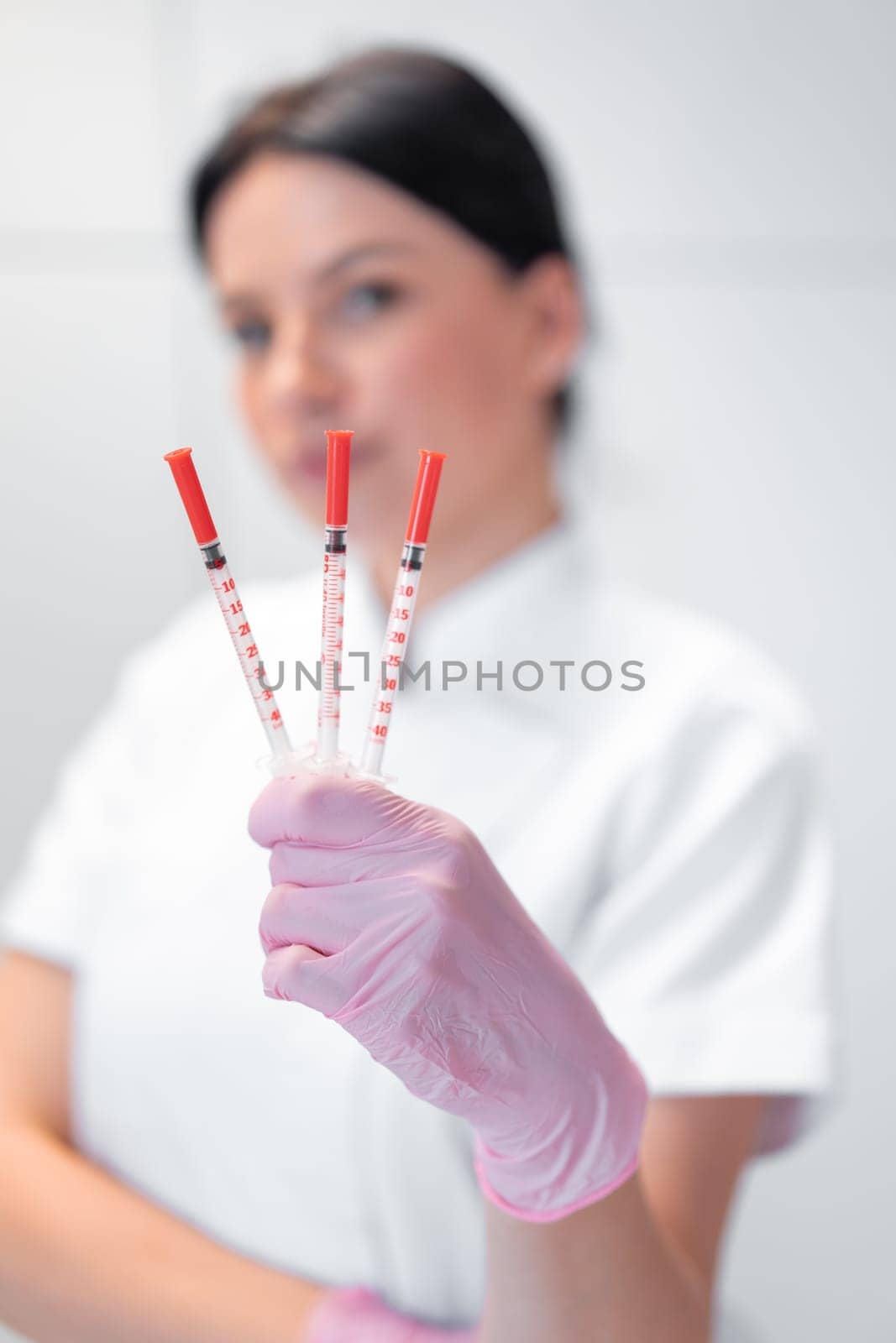 Blurry portrait of cosmetologist woman holding three syringes in hand. The concept of professional rejuvenating skin care. Female dermatologist showing injections in beauty clinic.