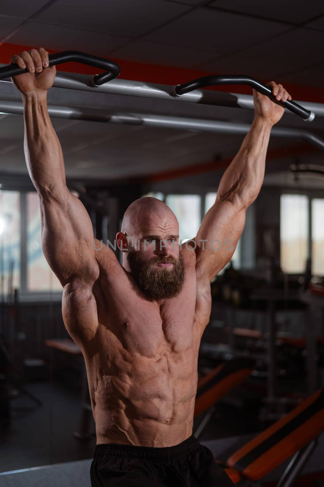 A Caucasian man hangs on a horizontal bar and raises his legs. Vertical photo