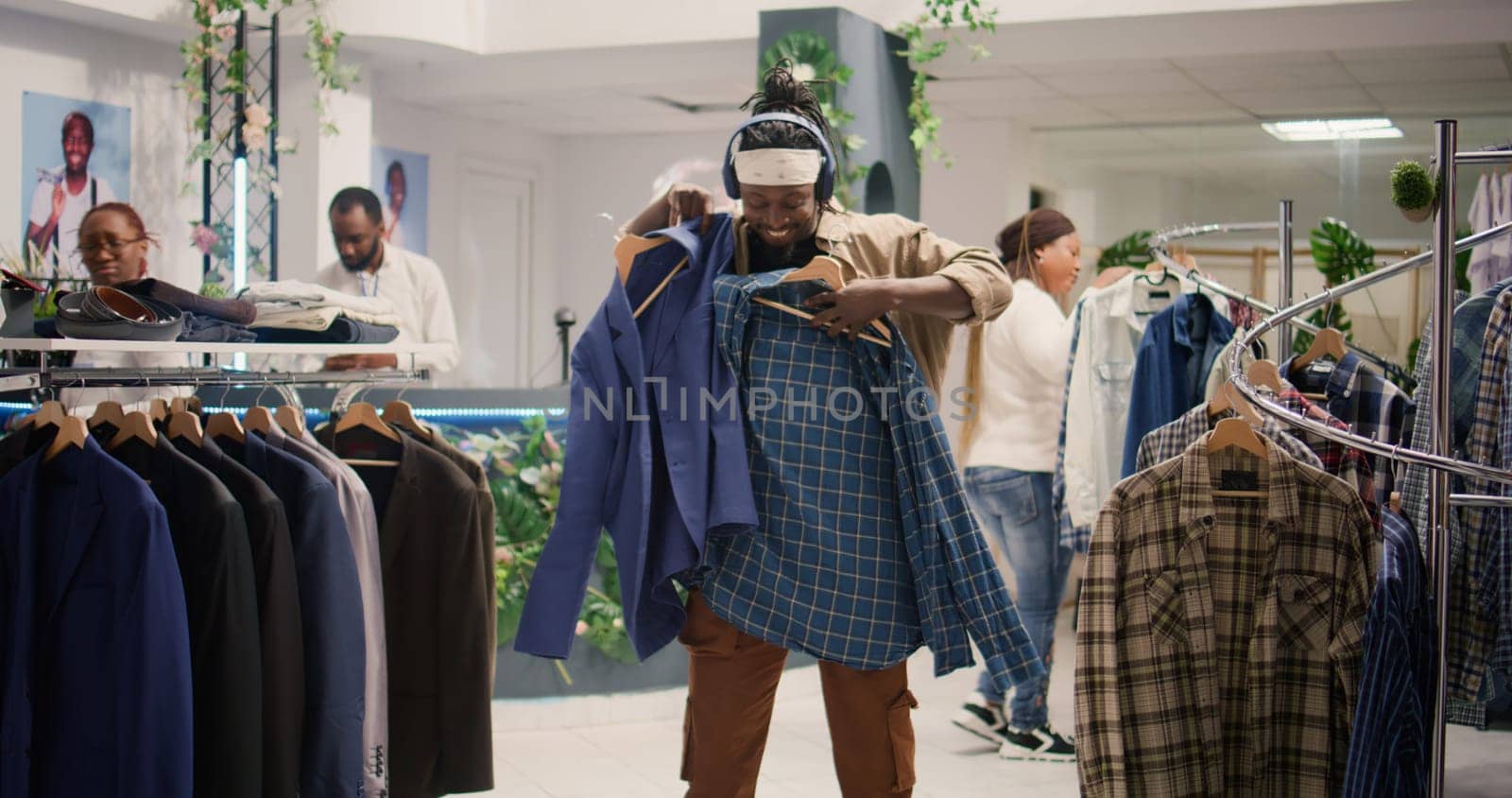 Man listening to music and dancing while looking at elegant clothes in clothing store, trying to determine if materials are qualitative. Client having fun fashion boutique while analyzing garments