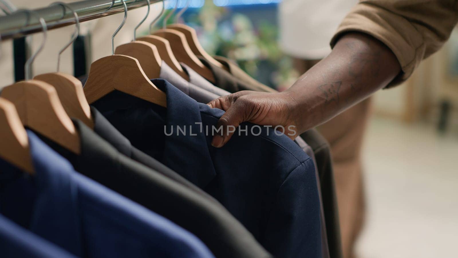 Customer in thrift shop browsing through clothes on racks to find perfect outfit. Close up shot of client in second hand clothing store doing shopping, wanting to purchase elegant blazer