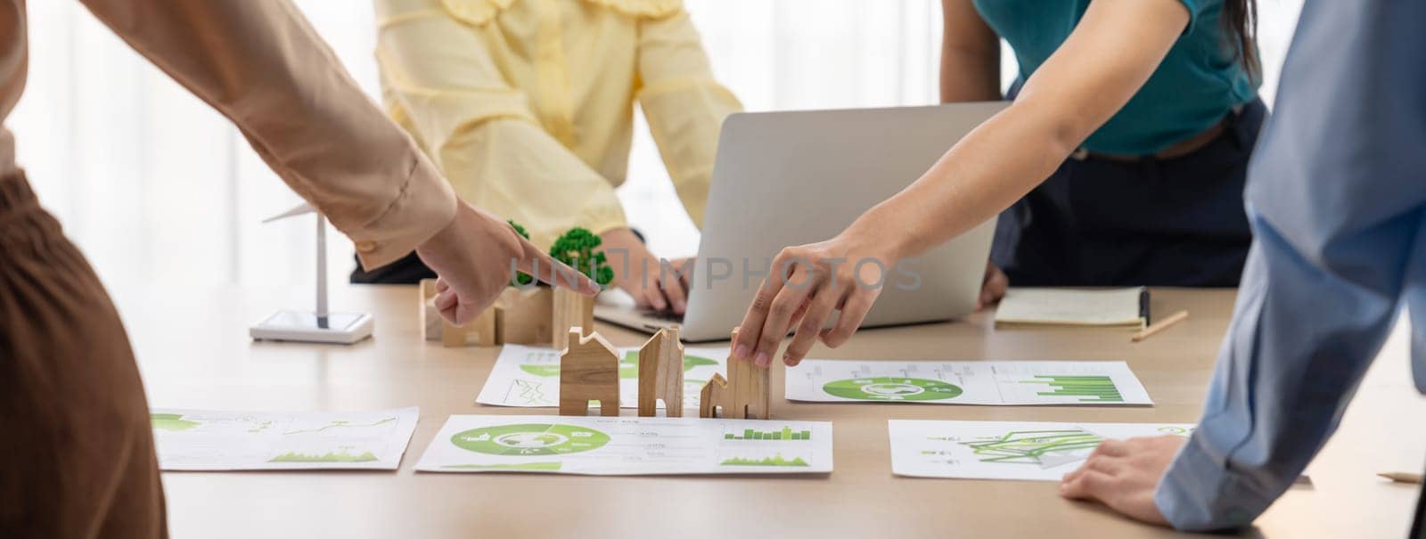 Wooden block represented green city and wind mill represented renewable energy was placed at center of green business meeting table with environmental document. Green business concept. Delineation.