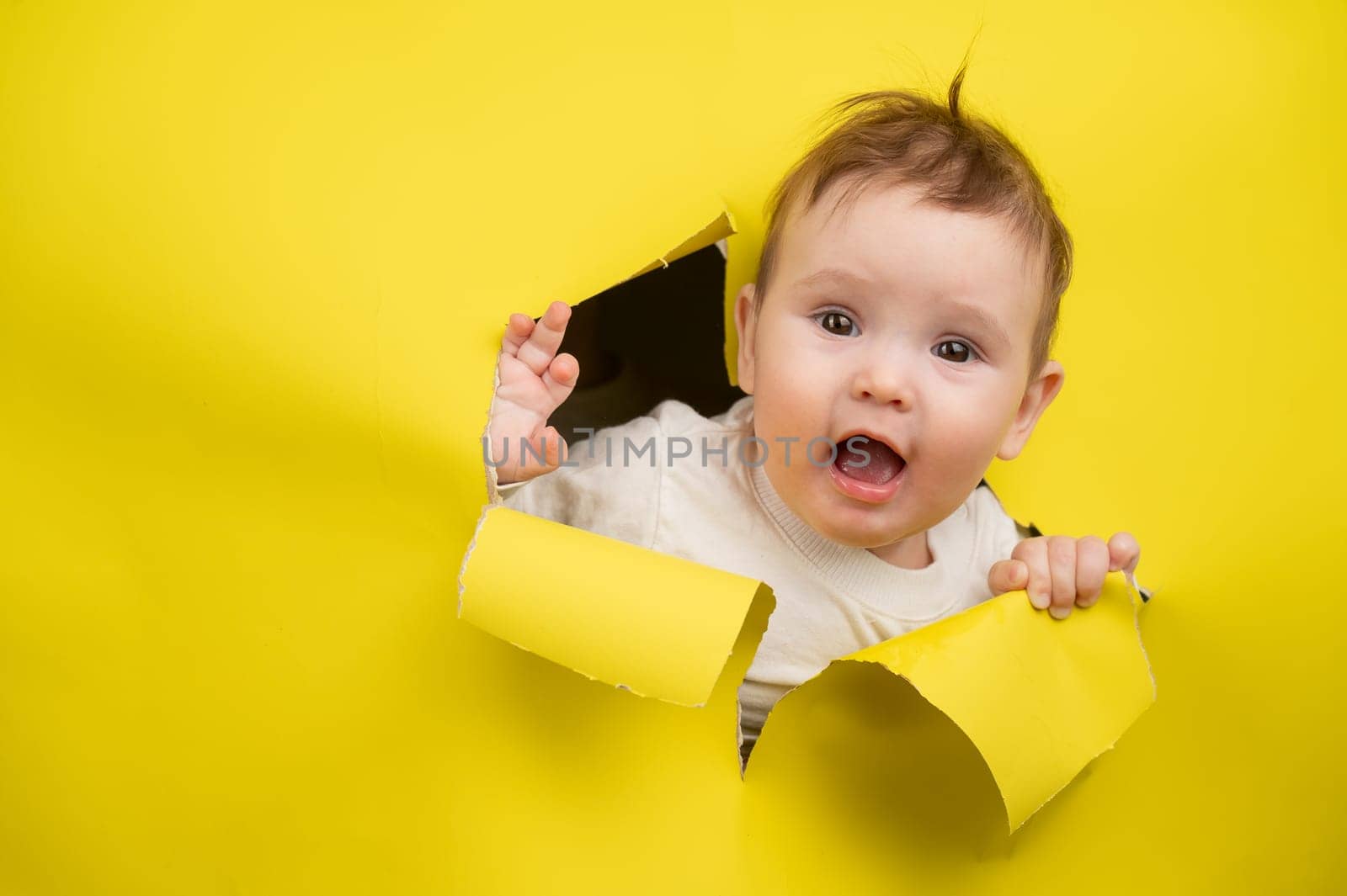 Cute Caucasian baby sticking out of a hole in a paper yellow background
