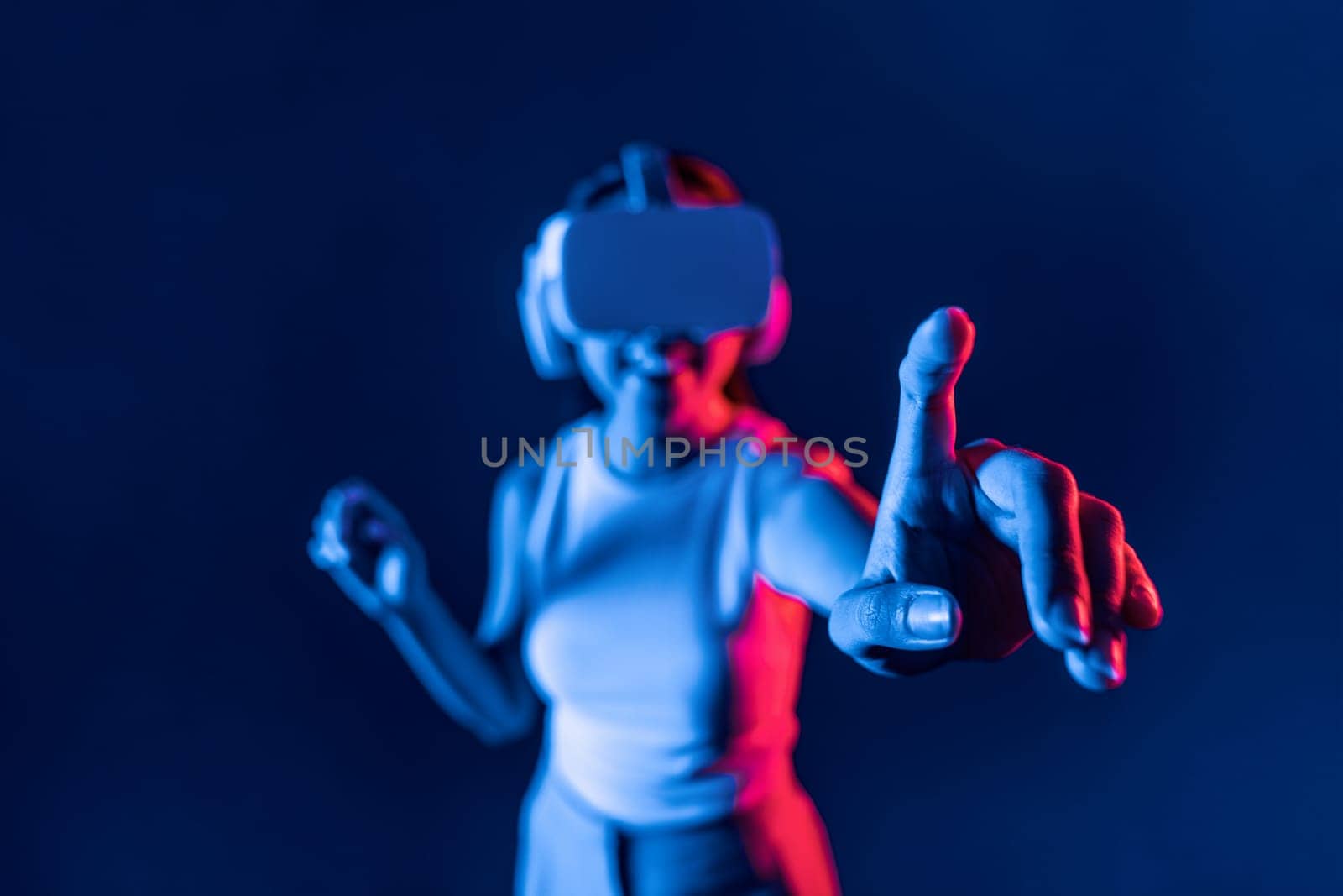 Smart female standing in cyberpunk neon light wear VR headset connecting metaverse, futuristic cyberspace community technology. Elegant woman use finger point generated virtual object. Hallucination.