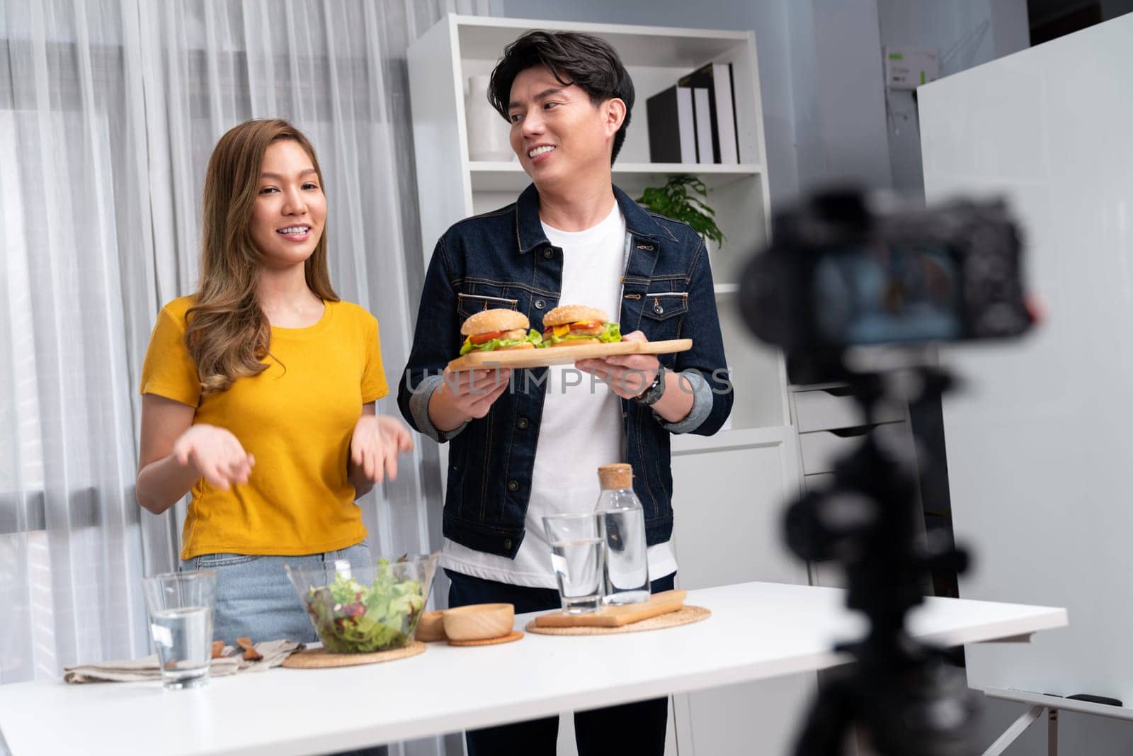 Chef influencers presenting on cooking show on social media channel serving double big hamburger set with dressing on camera recording. Bun bread wholegrain and salad placing menu homemade. Infobahn.