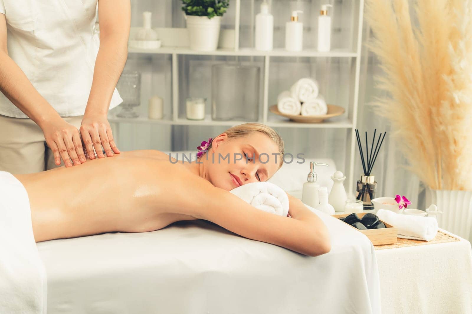 Caucasian woman customer enjoying relaxing anti-stress spa massage and pampering with beauty skin recreation leisure in day light ambient salon spa at luxury resort or hotel. Quiescent