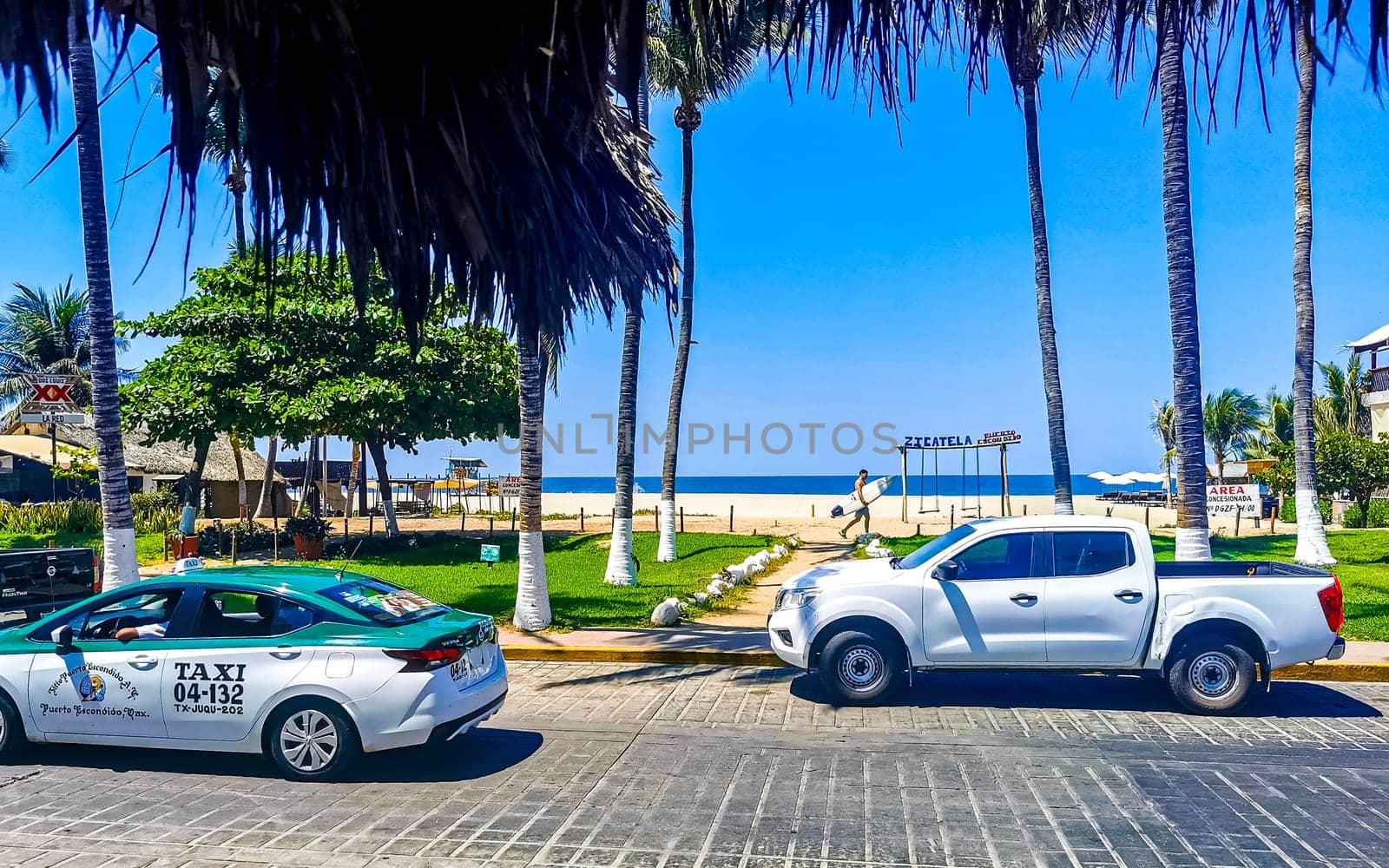 Typical beautiful colorful tourist street road and sidewalk at coast beach with city life cars traffic buildings hotels bars restaurants and people in Zicatela Mexico.