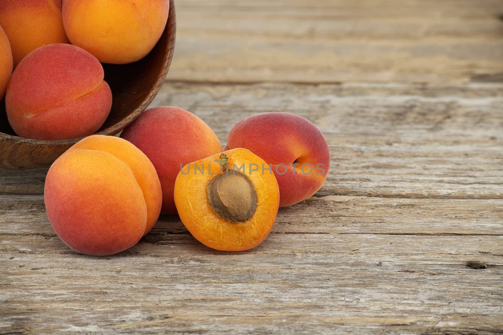 Group of fresh whole apricots and one cut in half to reveal its interior, rustic wooden table