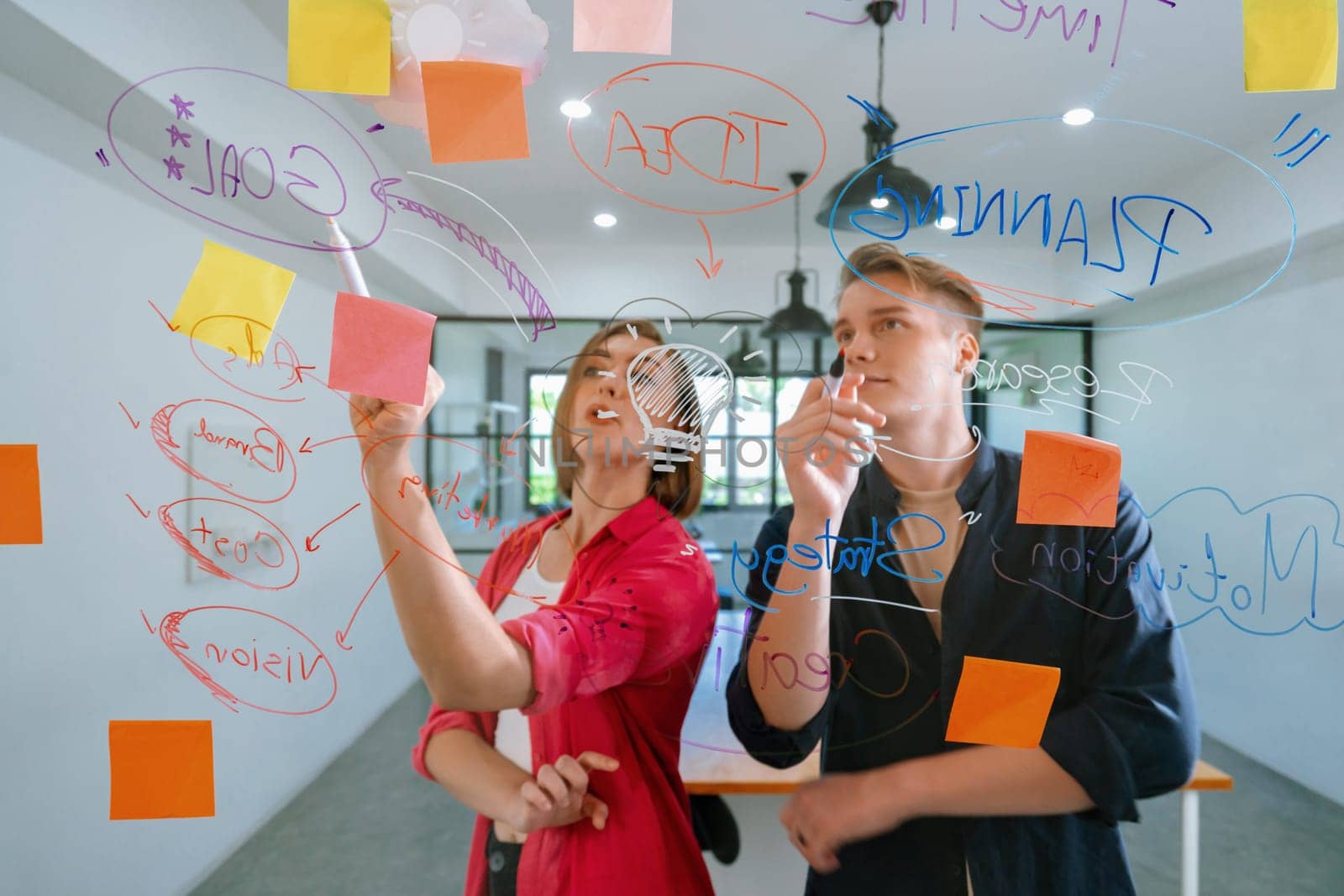 Couple of young creative start up business people brainstorming idea and solving problems by using sticky note and mind map at glass board, meeting room. discussing, working together. Immaculate.